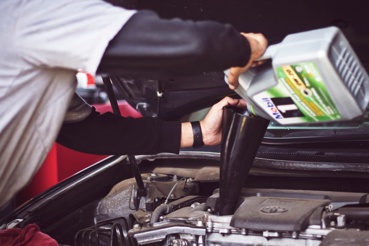 Mechanic pouring oil into a car engine during a service